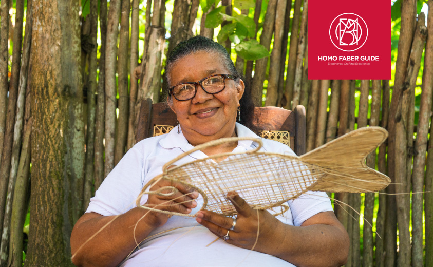 Foto de la artesana Edilsa Baldomino tejiendo una artesanía con forma de pescado en fibra de iraca